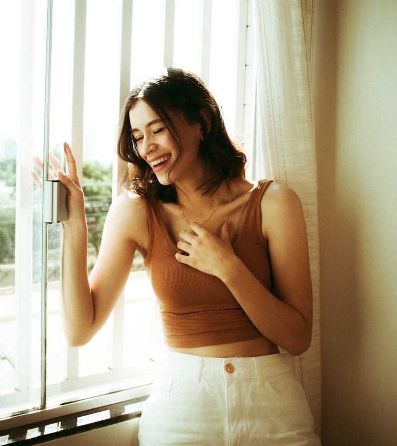 Smiling person doing a gentle morning stretch by a window.